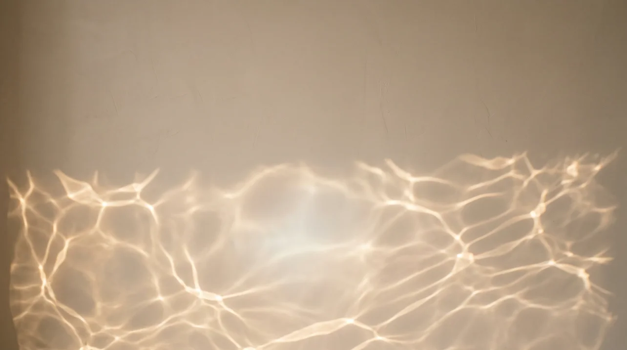 Rippling reflections of champagne light on a bone colored wall